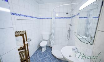 A modern bathroom with white tiles and blue accents. It features a shower, a toilet, and a sink.