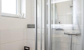 A modern bathroom with a shower and a toilet. The walls are tiled in light colors, and there is a window for daylight.