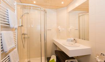 A modern bathroom with a shower cabin and a sink. The walls are brightly tiled, and the furnishings are simple and elegant.