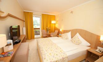 A cozy hotel room with a double bed and a quiet balcony. The windows are covered with yellow curtains and there are modern furnishings.