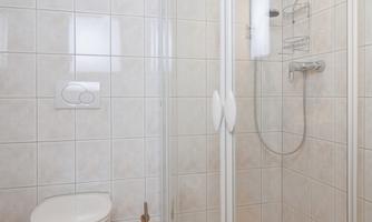 A modern bathroom with a shower in a glass enclosure and a toilet. The floor is tiled and there is a yellow towel on the floor.
