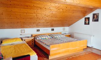 A cozy bedroom with a wooden ceiling and two beds. Some pictures hang on the wall and the floor is covered with a carpet.