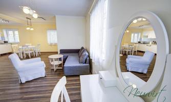A bright and modern living room with a sofa, a mirror, and a table. White furniture and large windows create a friendly atmosphere.