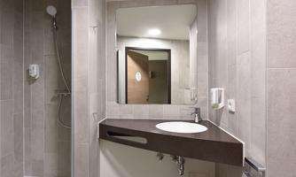 A modern bathroom with bright tiles and a large mirror. There is a shower and an elegant sink on a dark countertop.