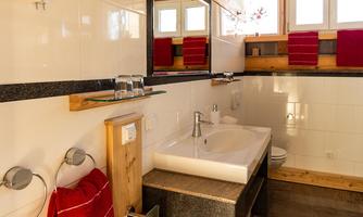A modern bathroom with an elegant sink and wooden details. Red towels and large windows create a bright, friendly atmosphere.