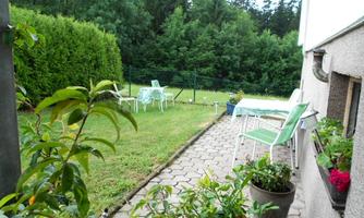 A cozy garden area with lawn and some garden furniture. In the background, trees can be seen providing a green backdrop.