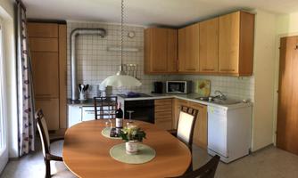A modern kitchen with wooden cabinets and a dining table. The equipment includes a stove, a microwave, and a refrigerator.
