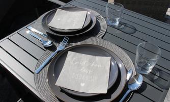 A beautifully set table with dark plates, cutlery, and glasses. On the plates, there are napkins with a beautiful print.