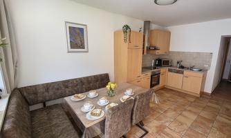 A modern kitchen with a dining area and brown upholstered furniture. On the table are plates and asmall flower vase.