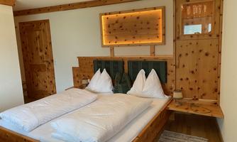 A cozy room with a double bed and traditional wooden furniture. A lighted mirror hangs on the wall, and the room radiates a warm atmosphere.