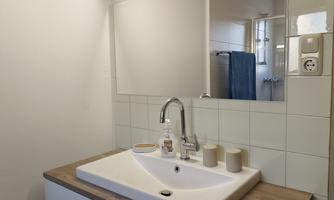 A modern bathroom with a stylish sink and wooden details. The space is bright and well-lit with a large mirror.