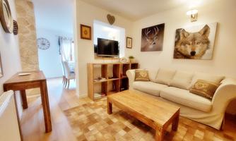 A cozy living room with a beige sofa, a wooden table, and a television. Decorative pictures hang on the walls, including a wolf and a deer.