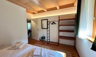 A modern bedroom with two beds and wooden ceilings. There is a clothes rack and shelves in the corner.