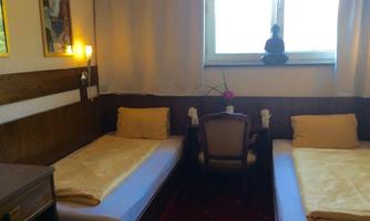 A cozy room with two single beds and a combination of chairs. The window provides natural light and a relaxed atmosphere.