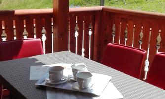 A cozy balcony with a table and red chairs. On the table, there are coffee cups and a beautiful view of the green hill.