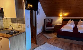A cozy accommodation with a small kitchen and a double bed. The room features a modern design and warm lighting.