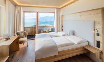 A modern bedroom with a large bed and wooden furniture. Through the windows, one looks out onto a picturesque landscape.