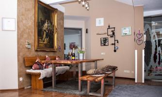 A cozy dining area with a large table and a bench. A large painting hangs on the wall, and the decor is modern.