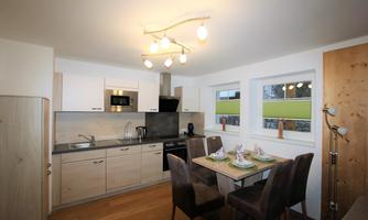 A modern kitchen with wooden cabinets and stainless steel appliances. A table with seating is also available.