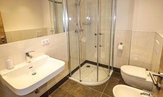 A modern bathroom with a shower and two toilets. The design is bright and clean with modern sanitary fixtures.