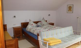 A cozy bedroom with a large double bed and wooden cabinets. A sitting area with a light blue sofa and a yellow towel is also available.