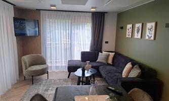 A modern living room with a comfortable sofa, a table, and large windows. The walls are painted in warm colors and there are decorative pictures.