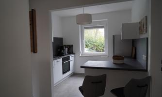 A bright kitchen with modern appliances and a small dining area. The view from the window shows green plants outside.