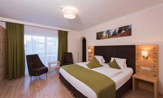 A modern hotel room with a double bed and two comfortable chairs. Large windows provide plenty of daylight and a pleasant atmosphere.