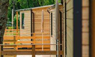 Modern wooden cabins with verandas in a green environment. The cabins have awnings for sun protection.