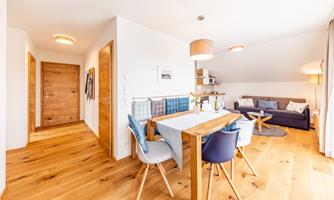 A bright and modern living room with a dining area and a comfortable couch. The wooden floor and warm colors create an inviting atmosphere.