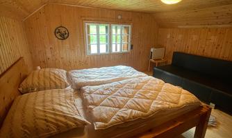 A cozy bedroom with a wooden bed and two large pillows. The walls are made of wood, and there is a window with a view outside.