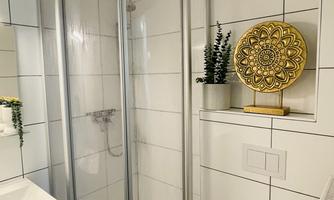 A modern bathroom with a glass shower and white tiles. On the left is a sink and on the right is a toilet.