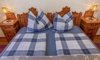 A cozy bedroom with a large bed and checkered pillows. Next to the bed are two nightstands with small lamps.