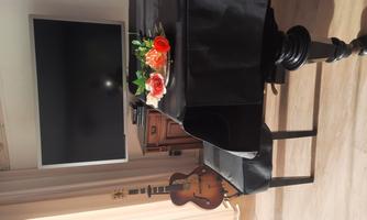 An elegant piano with a black tablecloth and a flower vase on top. In the background, there is a television, and a guitar leans against the wall.