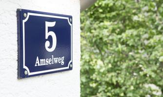 A house number sign with the number 5 and the street name "Amselweg". In the background, green leaves can be seen.