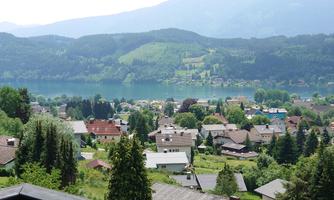 A picturesque landscape overlooking a village by the water. Gentle hills and green forests surround the houses.