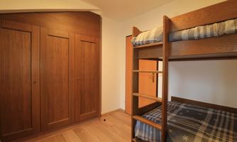 A simple room with a bunk bed and a wardrobe. The walls are bright and the floor is made of wood.
