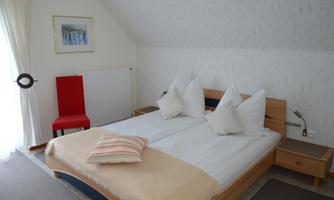 A cozy bedroom with a double bed and two pillows. A red chair and a window with curtains are also visible.