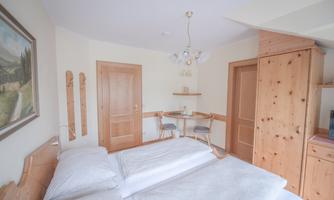 A cozy bedroom with two beds, wooden cabinets, and a small table. The walls are light and there is a beautiful painting.
