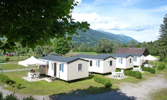 A peaceful holiday resort with several modern mobile homes in a green environment. In the background, mountains and a clear blue sky can be seen.