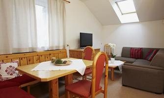 A cozy living area with a wooden dining table, chairs, and a sofa. The windows let in plenty of light, and the rooms are bright and inviting.