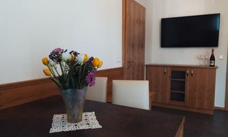 A cozy living room corner with a table and a vase full of flowers. In the background, there is a television and a sideboard.