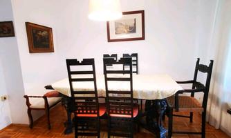 A dining room with a large table and several black chairs. Pictures are hanging on the wall and the room is brightly lit.