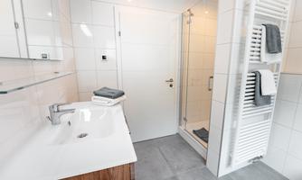A modern bathroom with a shower and a sink. The walls are brightly tiled and there are clean towels on the towel rack.