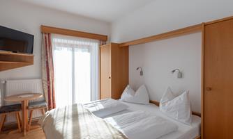 A cozy hotel room with a double bed and two pillows. There is a table and chairs as well as a television on the wall.
