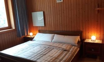 A cozy bedroom with wooden paneling. The bed is neatly made and there is soft lighting next to the bed.
