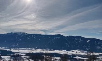 An impressive winter landscape with snow-covered mountains and a clear blue sky. The sun shines brightly over the valley.