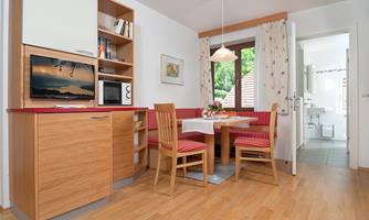 A cozy kitchen with a dining area for four people. The room is bright and friendly, with wooden flooring and a beautiful view outside.