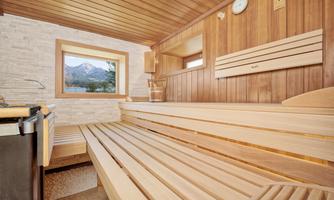 A modern sauna with a wooden bench and window that offers a view of the mountains. The walls are made of wood and stone, creating a cozy atmosphere.