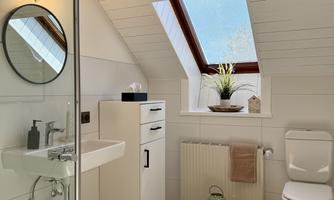 A modern bathroom with a skylight and bright tiles. The room is equipped with a shower, a sink, and a toilet.